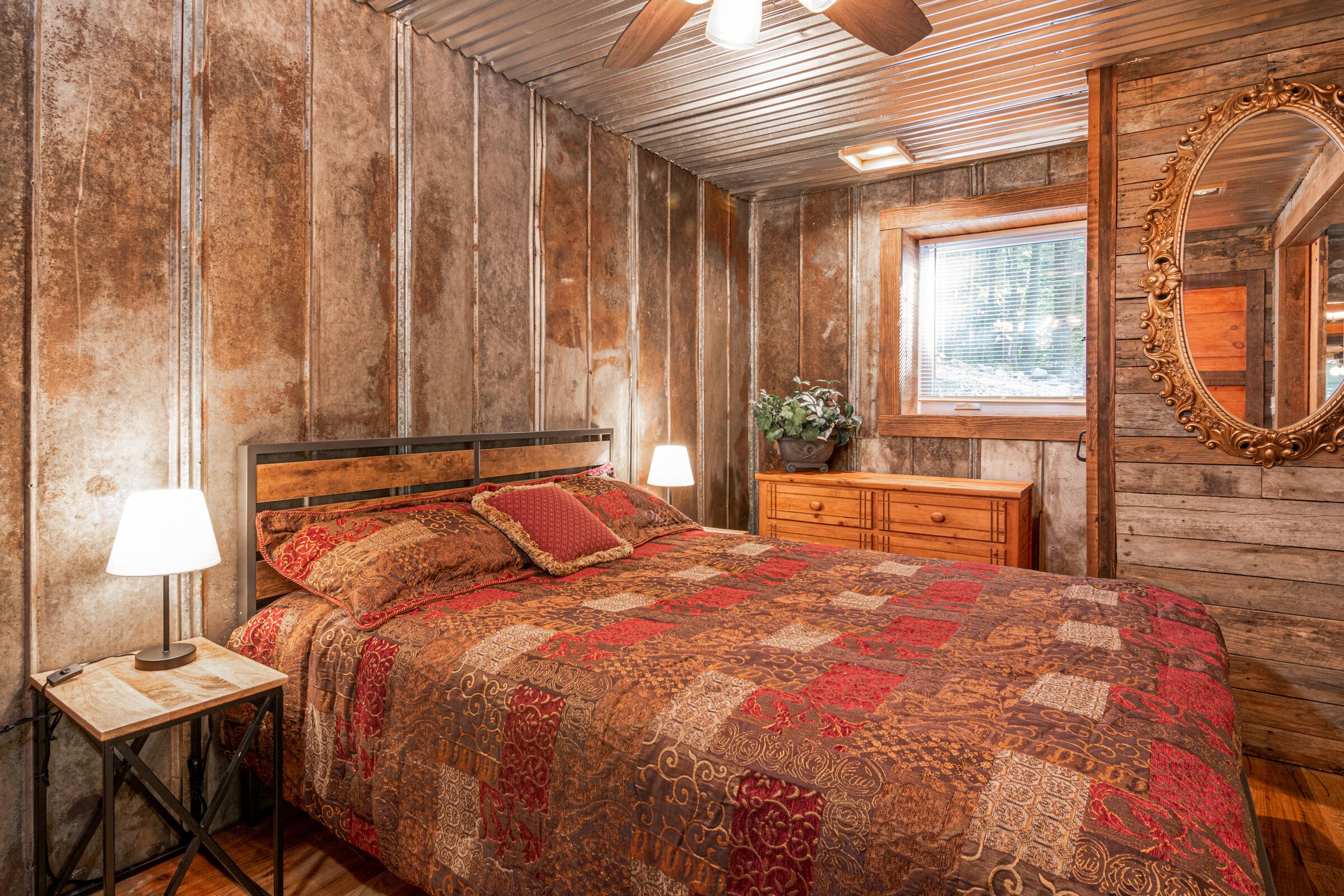 A rustic bedroom with a wooden bed, two bedside tables with lamps, a dresser, and a large mirror.