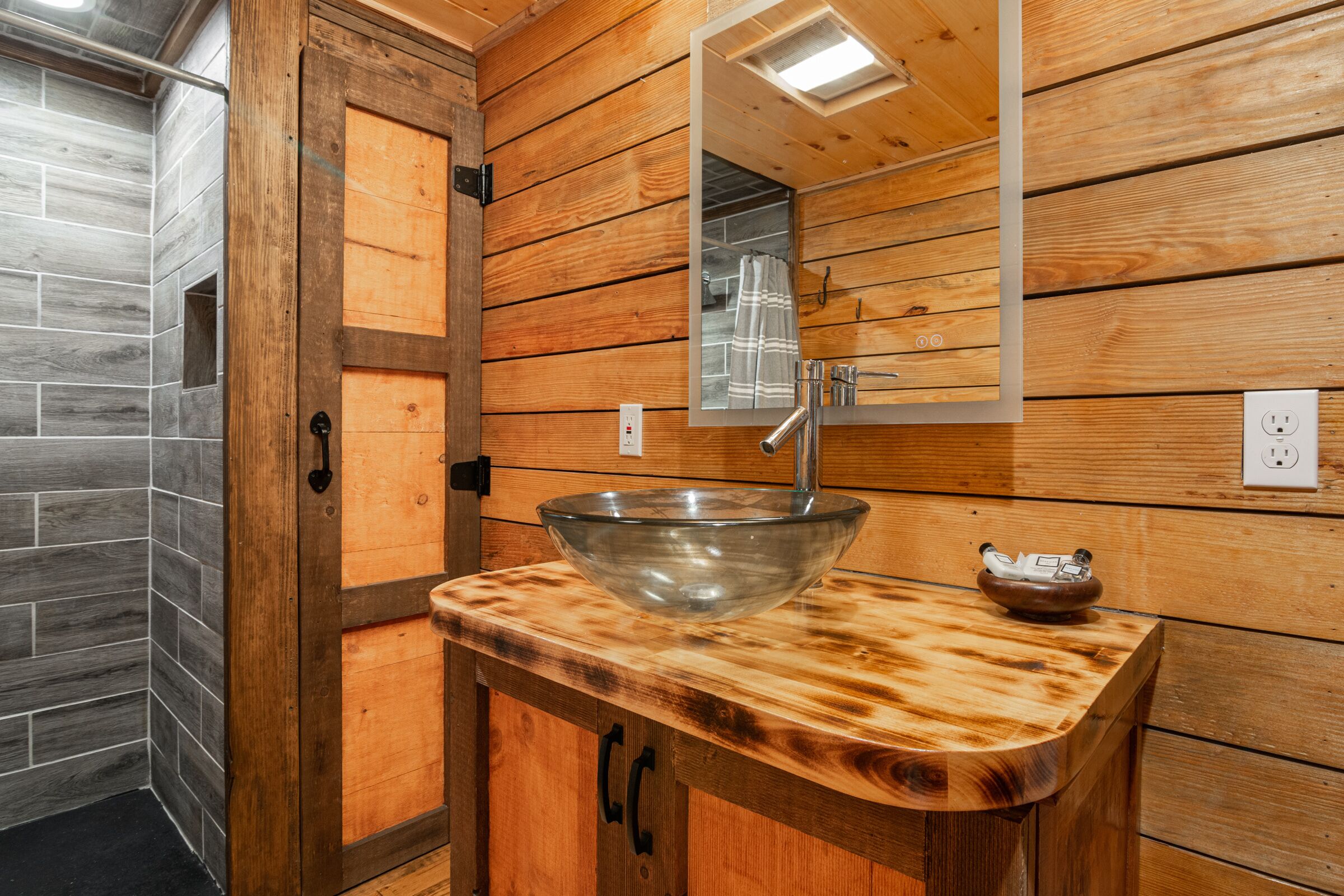 A wooden bathroom with a glass bowl sink, a mirror, and a wooden cabinet.