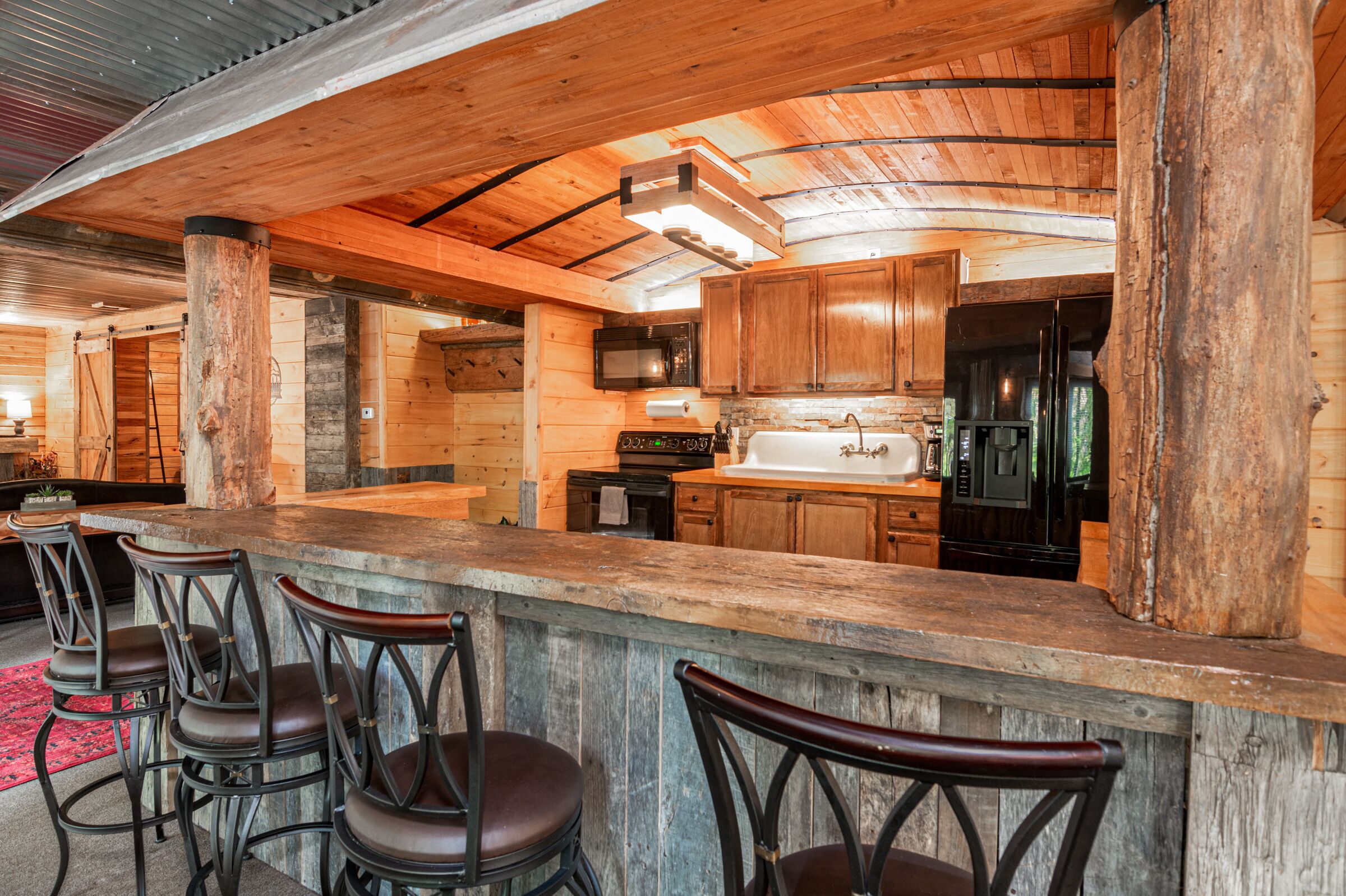 Una cocina rústica con armarios de madera, una isla grande con taburetes de bar y un refrigerador de acero inoxidable.