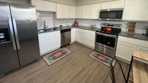 Une cuisine moderne avec des meubles blancs, des appareils électroménagers en acier inoxydable et un plancher en bois.