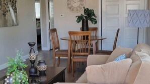 Un salon avec un canapé beige, une table à manger en bois avec des chaises, une horloge au mur et une plante en pot.