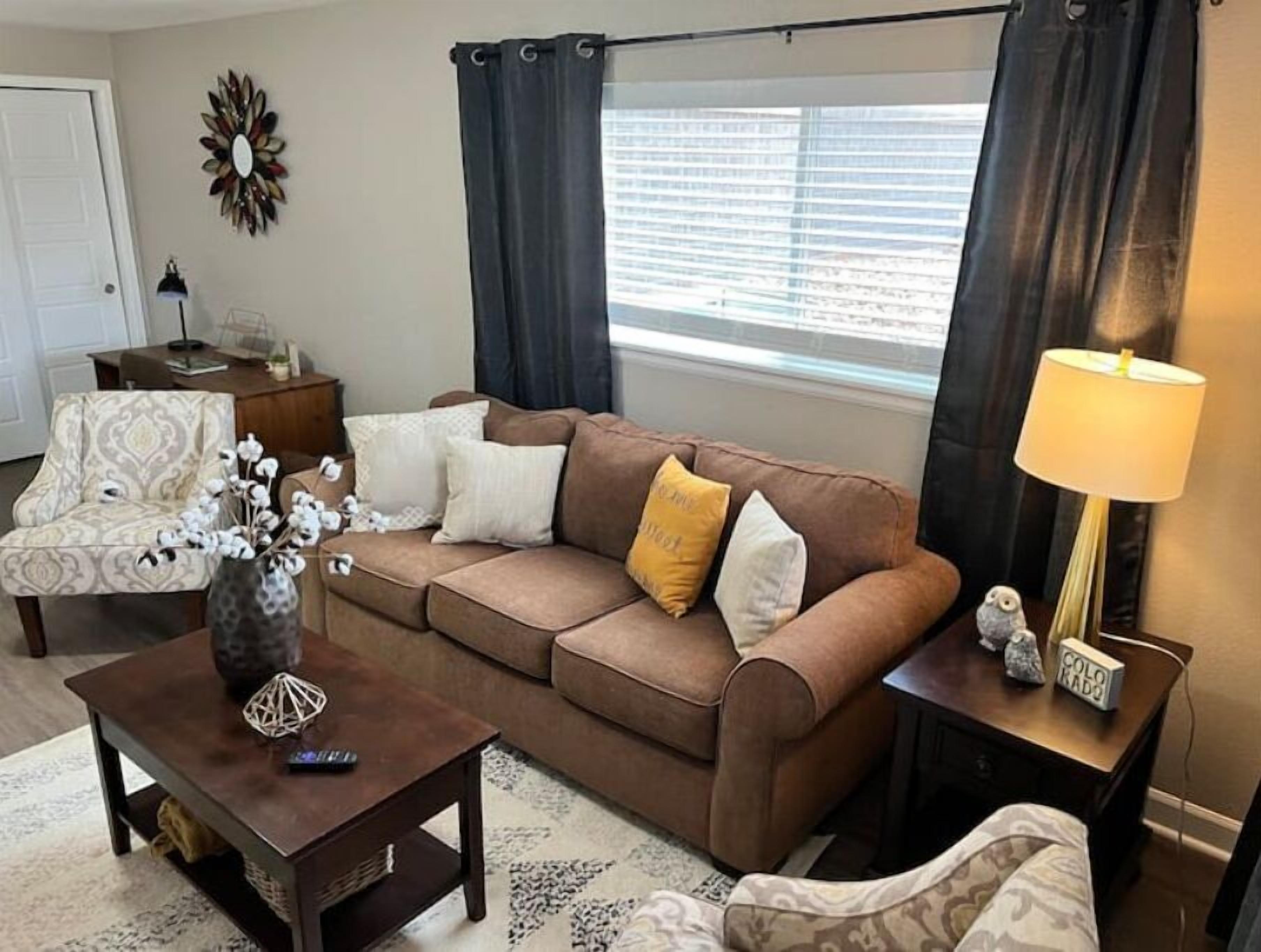 A living room with a brown sofa, patterned armchair, and a coffee table with a vase and a decorative item.