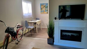 A living room with a fireplace, a television, a dining table with chairs, a bicycle, and a window with curtains.