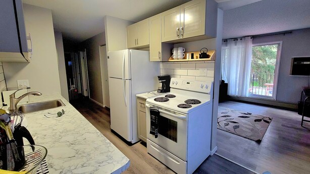 A compact kitchen with a refrigerator, stove, and sink. There is a window with a view of greenery outside.