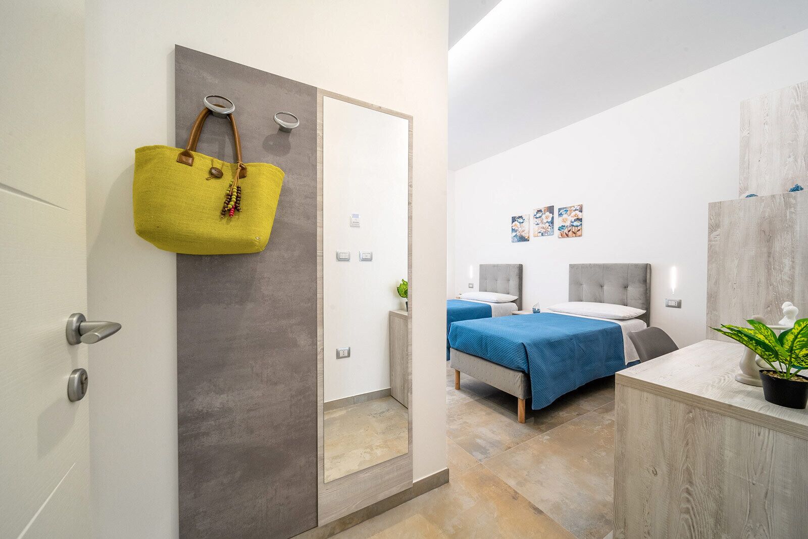 A modern hotel room with a bed, bedside tables, a mirror, and a plant.
