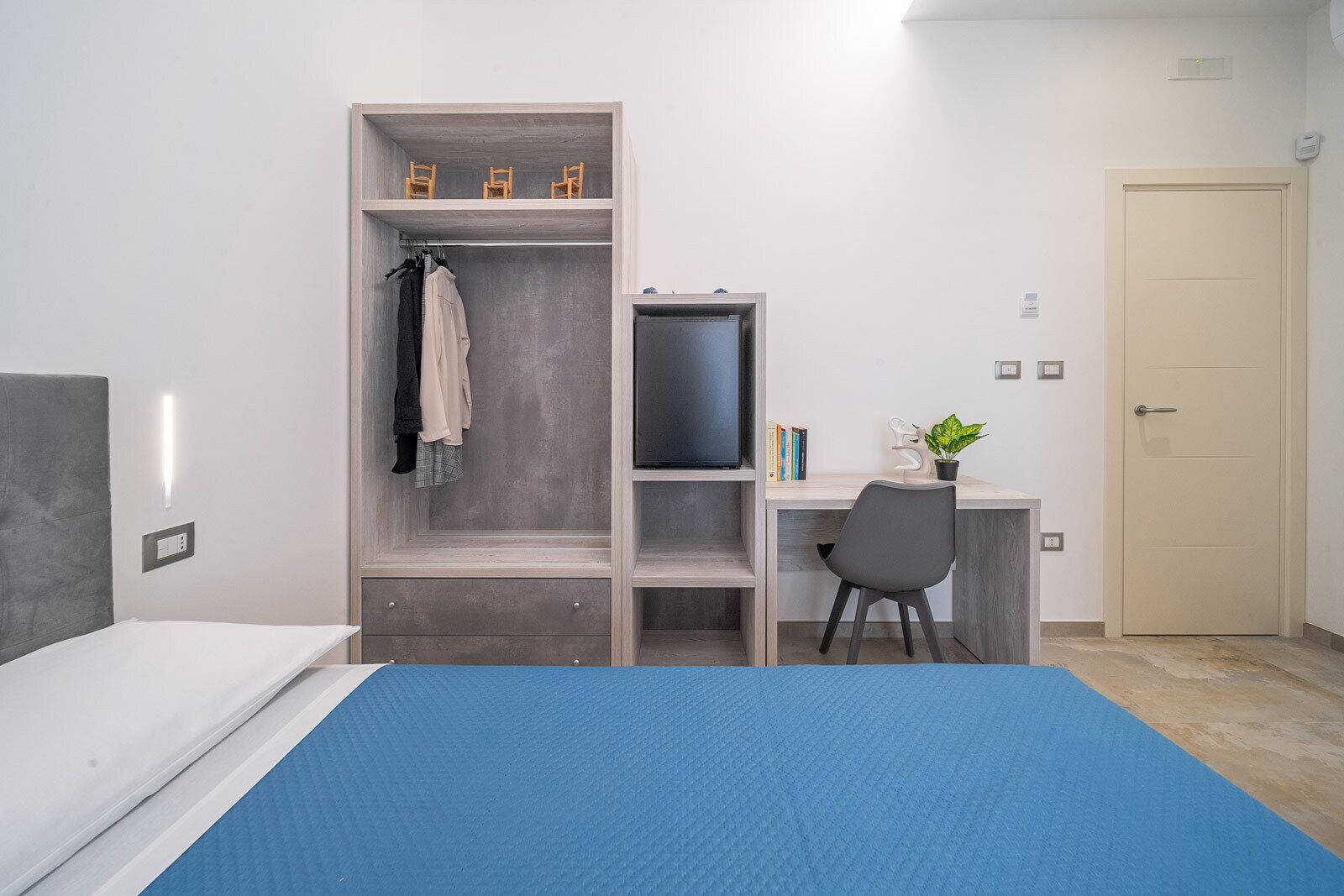 A bedroom with a bed, a desk with a chair, a wardrobe, and a door.