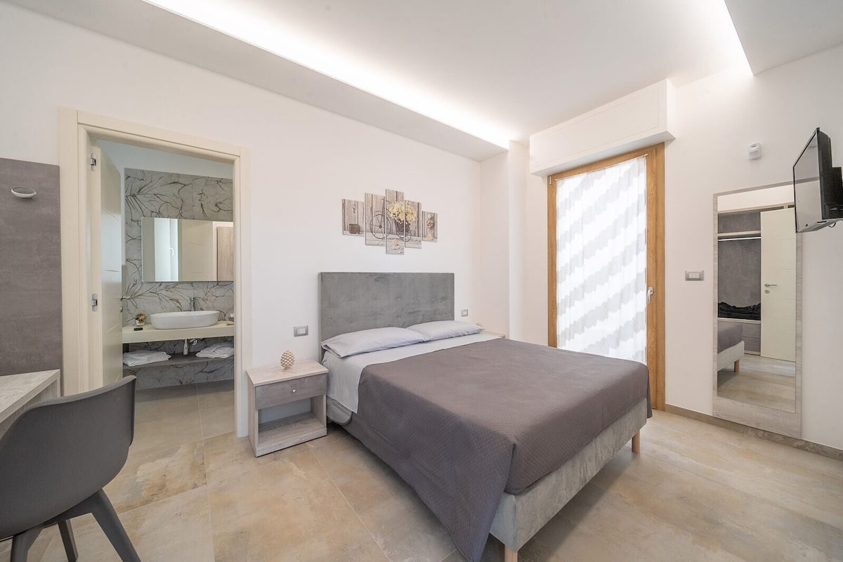 A modern bedroom with a bed, bedside table, and a desk area.