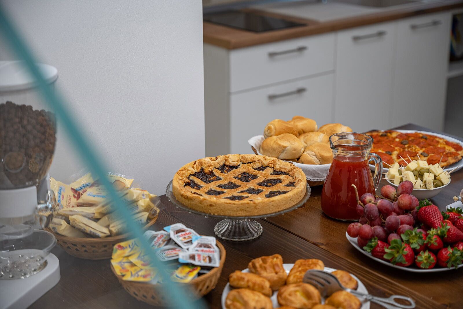 Ein Tisch mit verschiedenen Speisen, darunter Kuchen, Brötchen, Käsewürfel und Erdbeeren.