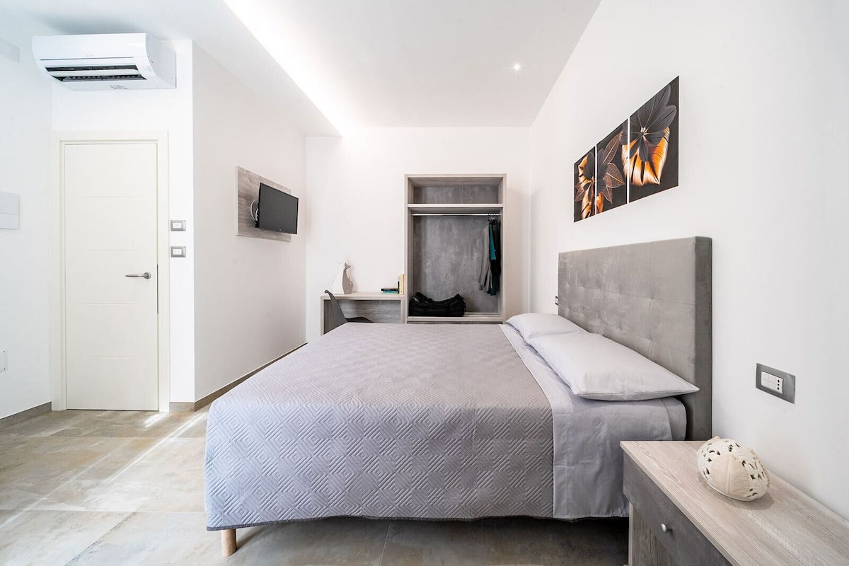 A modern bedroom with a bed, a wardrobe, a desk, and a TV.