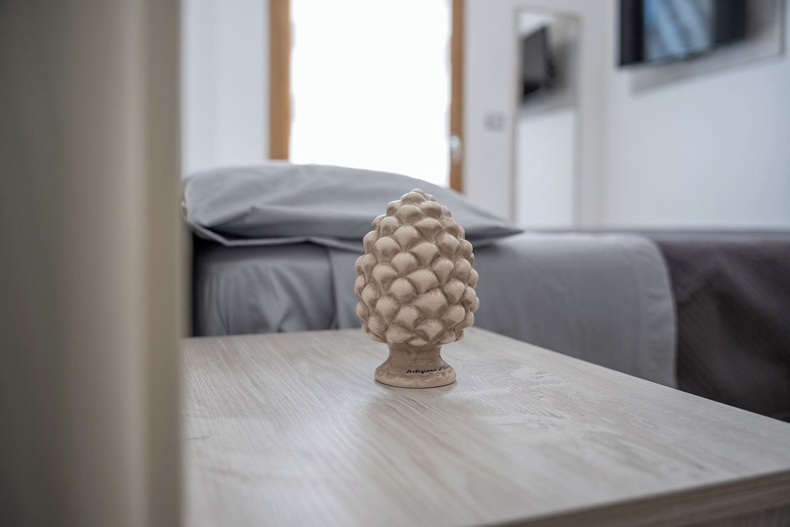 A pine cone sculpture on a wooden table in a modern room with a bed and a TV in the background.
