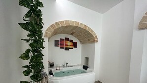 Um banheiro com banheira de pedestal, arco de tijolos, obra de arte na parede e planta em vaso.