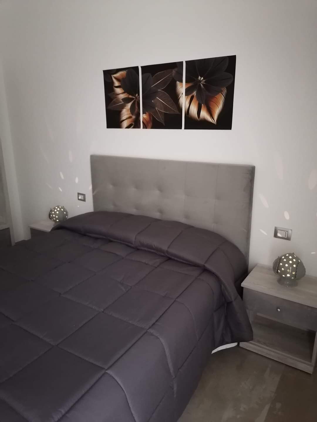 Un dormitorio moderno con una cama grande, cabecera gris y dos marcos de cuadros colgados en la pared.