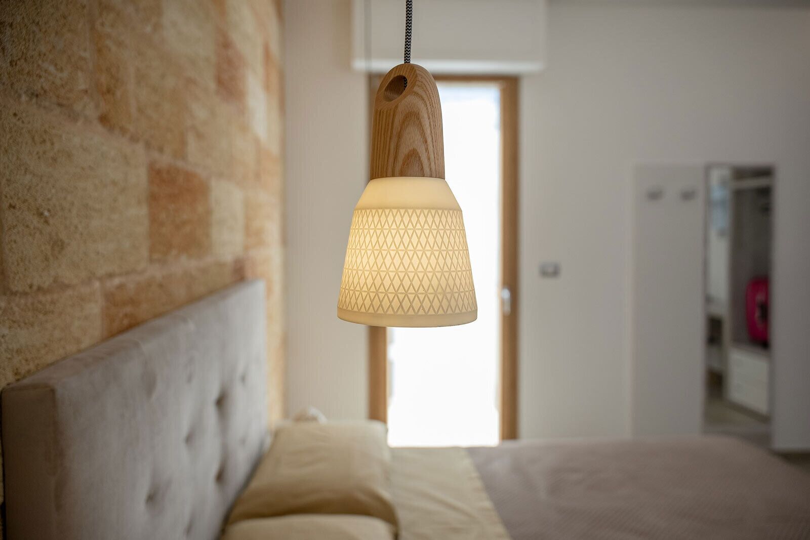 Een slaapkamer met een bed, een hanglamp en een bakstenen muur.