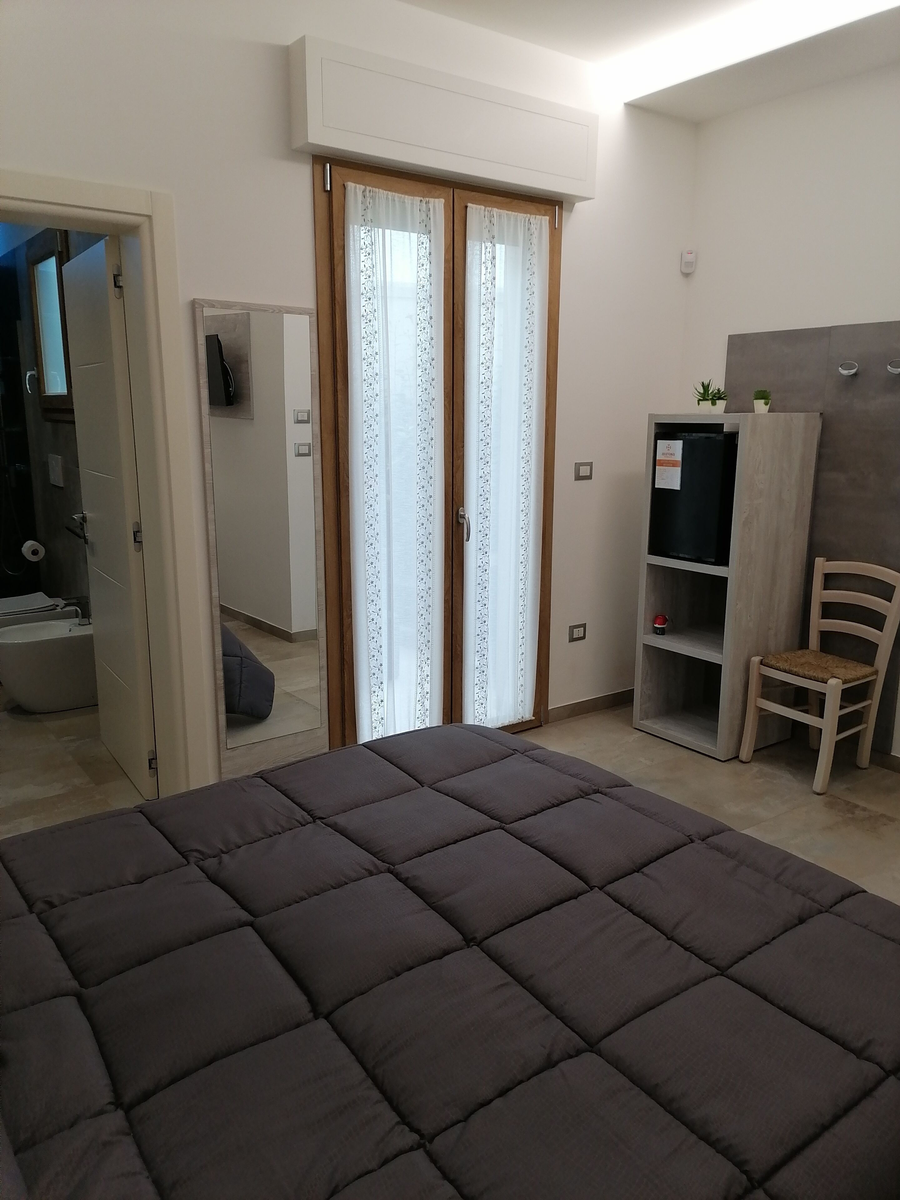A bedroom with a large bed, a wardrobe, a desk, a chair, and a bathroom visible through an open door.
