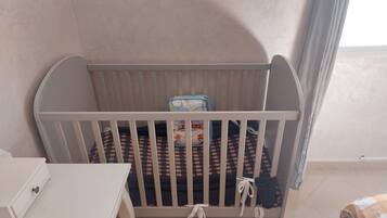 Un berceau blanc avec un matelas à carreaux, un petit bac de rangement et un jouet dans le coin.