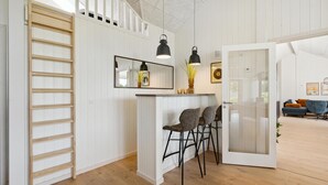 A modern kitchen with a wooden ladder, a bar area with stools, and a glass door leading to a living room with a sofa and a blue chair. - Gorgeous home in Rømø with sauna (Rømø)