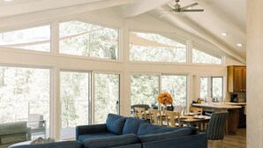 A spacious living room with a large blue sofa, a dining area with a table and chairs, and a kitchen area with wooden cabinets and a countertop.