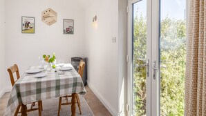 Un comedor con una mesa dispuesta para cuatro personas, un reloj y dos cuadros colgados en la pared.