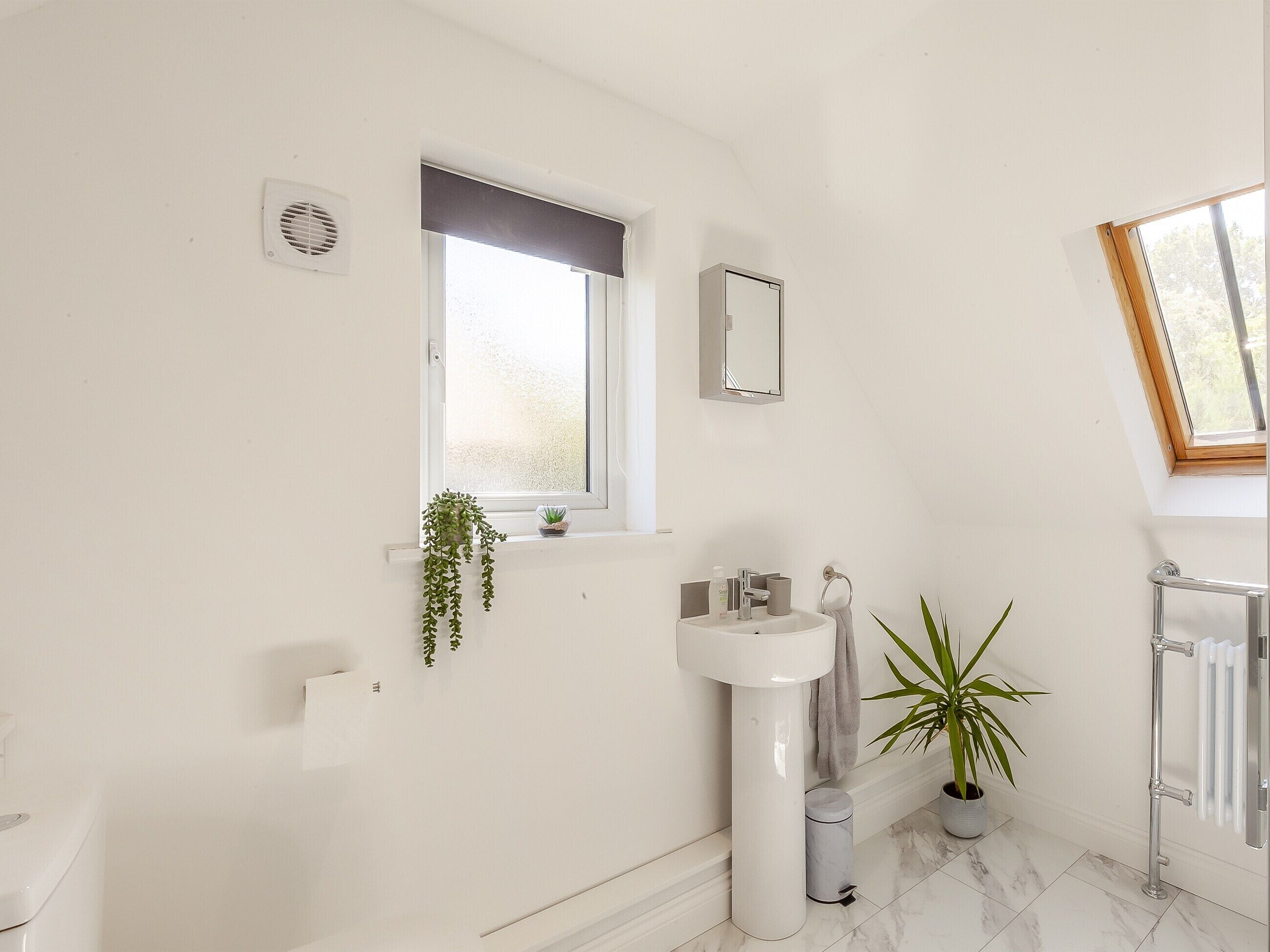 A modern bathroom with a white sink, mirror, and window.
