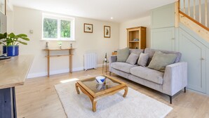 Un salón amplio con un sofá gris, una mesa de centro de madera y un ventanal con vistas a la vegetación.