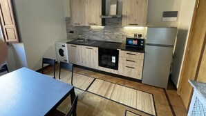 Cocina compacta con armarios de madera, microondas integrado y refrigerador de acero inoxidable.