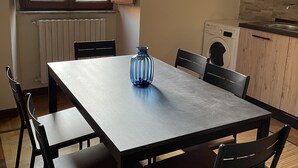 Un comedor con mesa y sillas, una ventana con vistas a edificios, una lavadora y una cocina con armarios de madera.