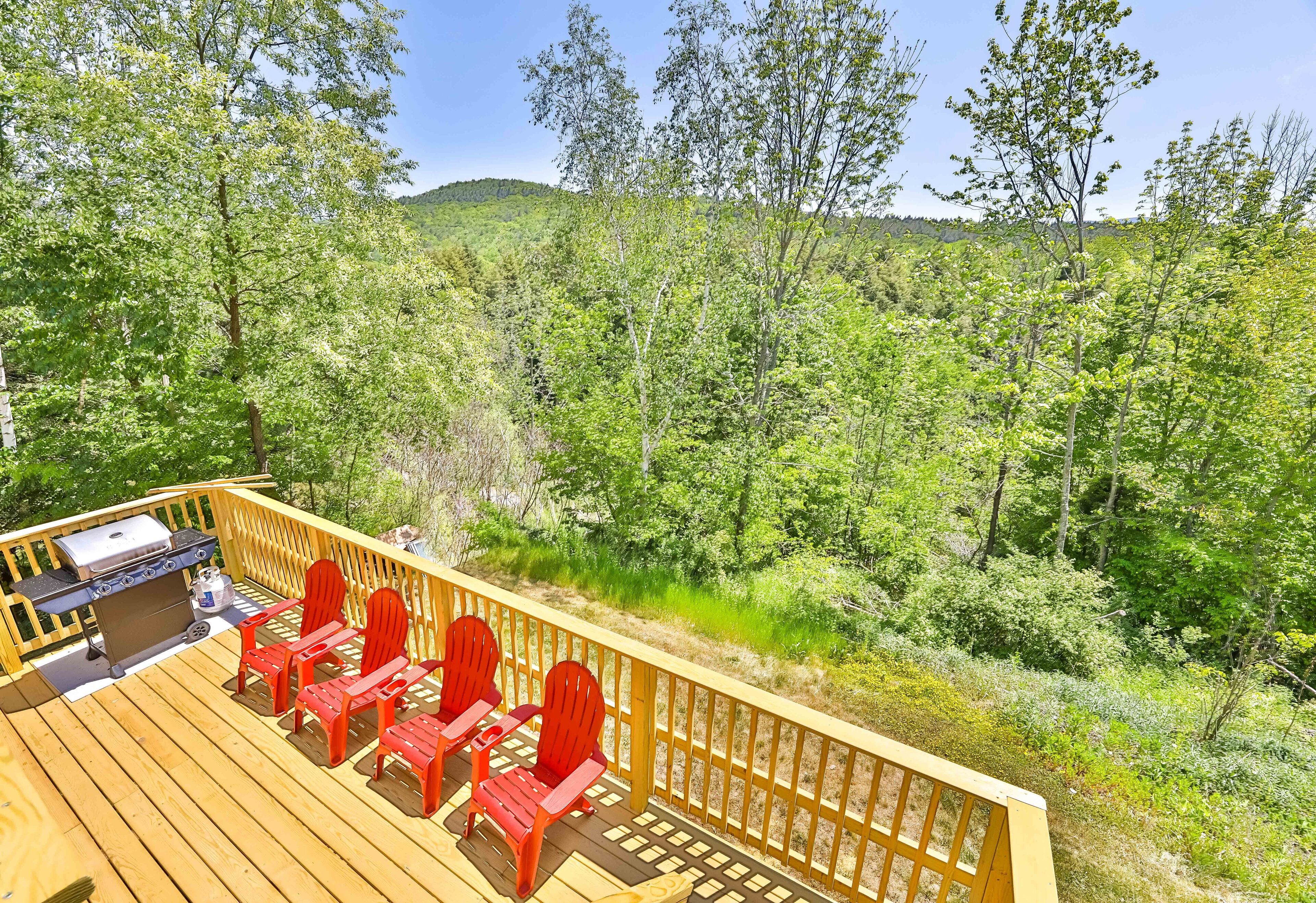 A deck with a grill and red chairs overlooking a forested area.
