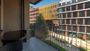 Un balcón con mobiliario de mimbre y una planta en maceta, con vistas a un edificio moderno con grandes ventanales y fachada de ladrillo.