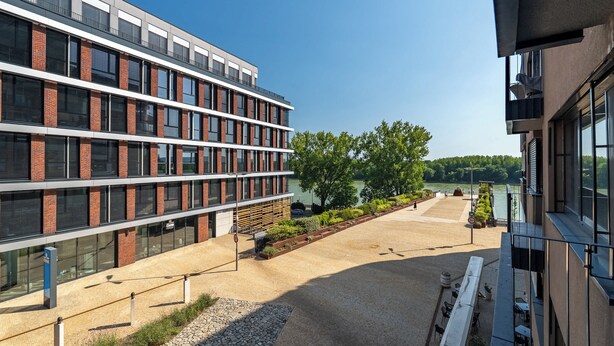 Un edificio moderno con un patio, ventanas amplias y vistas al río.