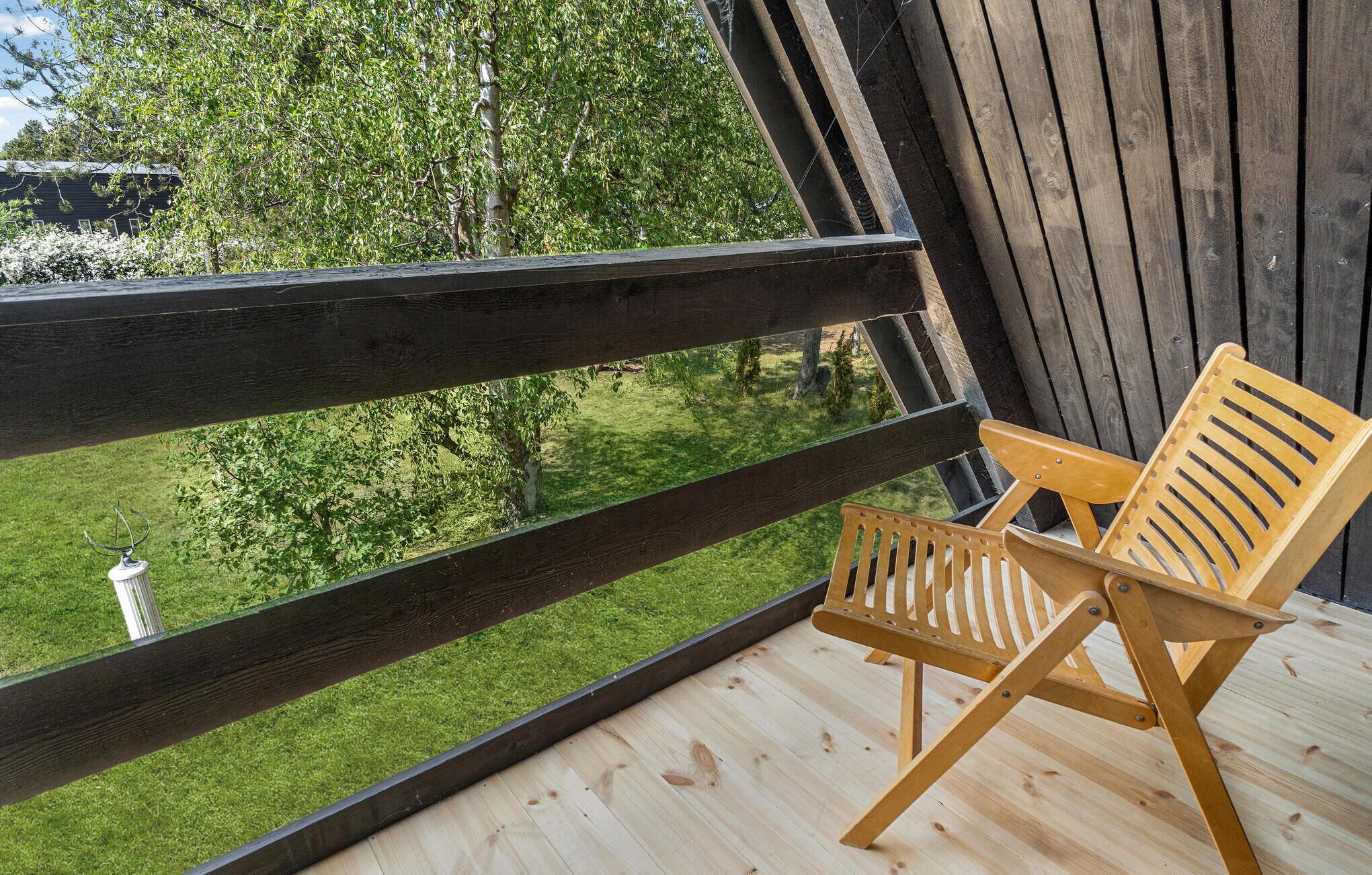 A wooden deck with a wooden chair and a view of a garden and trees.