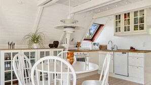 A kitchen with white cabinetry, a dining table with white chairs, a hanging light fixture, and a window with a view of trees.