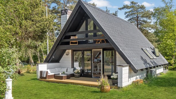 A modern A-frame house with a large glass door entrance, a deck with outdoor furniture, and a well-maintained lawn.