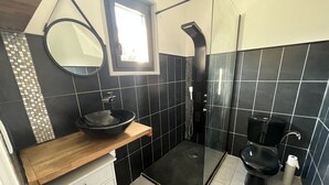 Un baño moderno con diseño de baldosas blanco y negro, un mueble de tocador de madera, un espejo redondo, un lavabo negro, una cabina de ducha de vidrio y un inodoro.