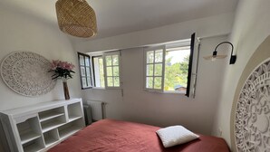 Un dormitorio con una cama grande, dos almohadas, una mesita consola blanca, un adorno en la pared y dos ventanas con cortinas.
