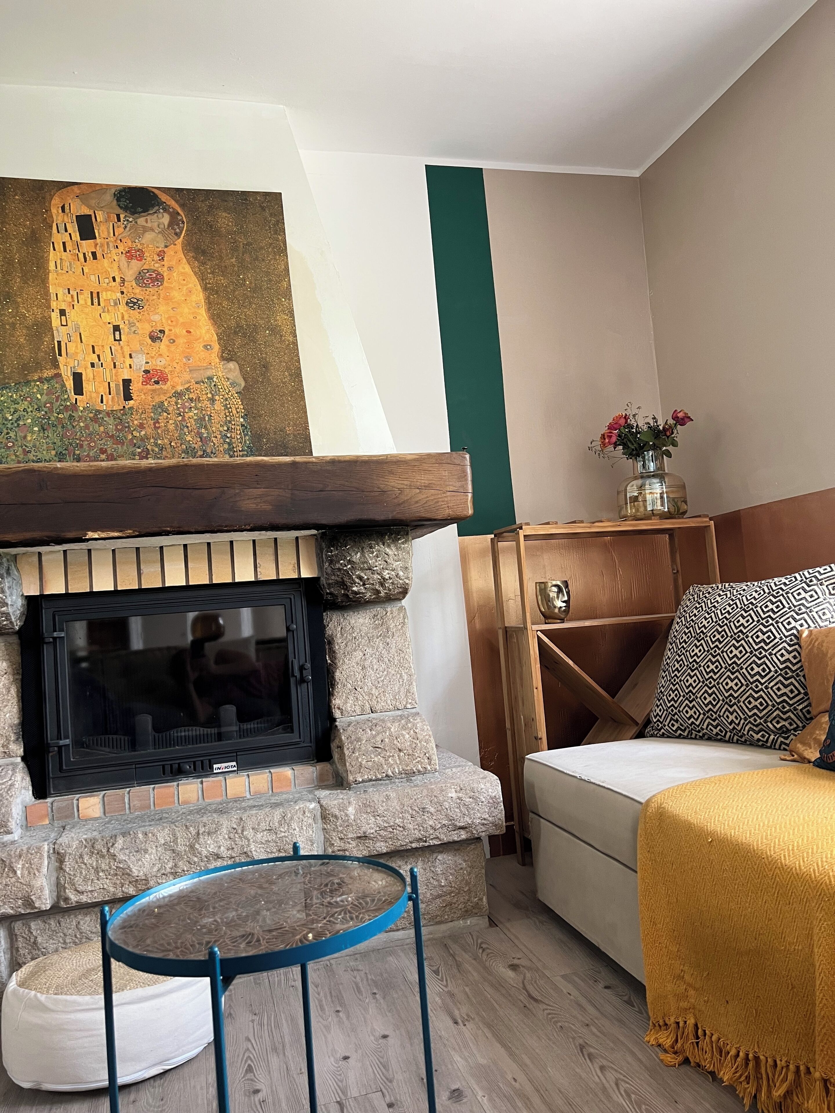 Una sala de estar acogedora con chimenea, un cuadro sobre ella, una mesa redonda y un sofá con una manta.