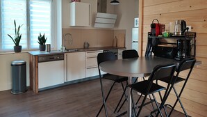 Una cocina moderna con una pared de acento de madera, un comedor con una mesa redonda y sillas, y un ventanal con persianas.