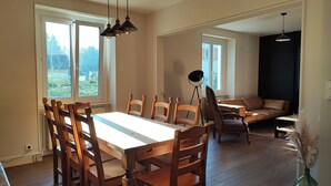 Un comedor amplio con una gran mesa de madera y sillas, un sofá de color oscuro, y una lámpara de pie.