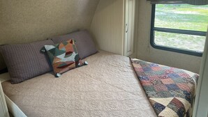 A bedroom with a bed, pillows, a quilt, and a window with a view of greenery. - Tree Top Ranch Glamping  (Larkspur)