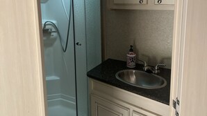 A bathroom with a shower, a sink, and a mirror. - Tree Top Ranch Glamping  (Larkspur)