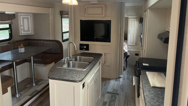 A compact RV kitchen with a built-in TV, a dining area with a bench, and a small kitchenette. - Tree Top Ranch Glamping  (Larkspur)