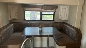 A compact RV interior with a kitchenette, a dining table, and built-in seating. - Tree Top Ranch Glamping  (Larkspur)