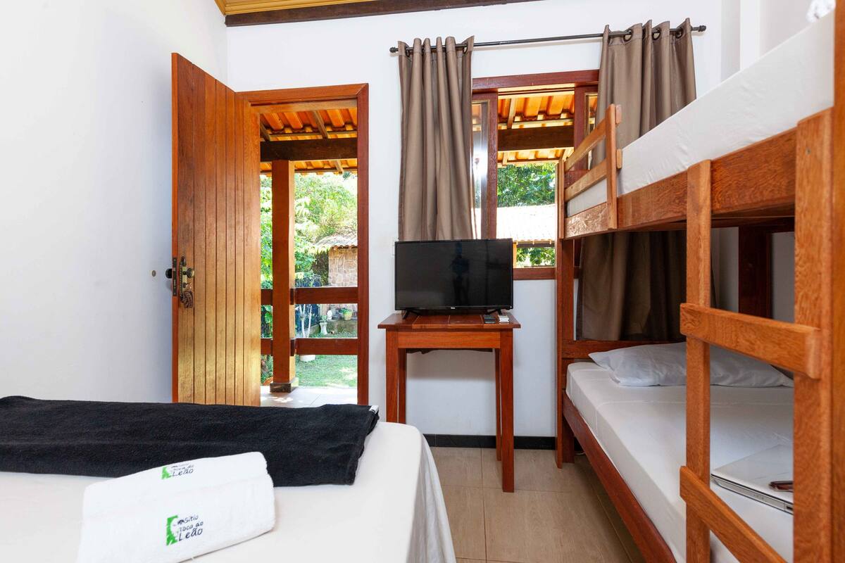 A room with a bunk bed, a single bed, a television on a wooden table, and a door leading outside.