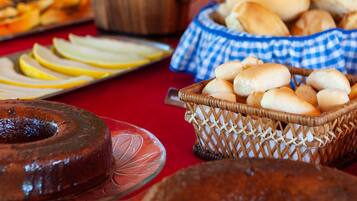 Una mesa de buffet con diversos productos horneados, incluyendo un pastel y panecillos, además de una cesta con manzanas en rodajas.