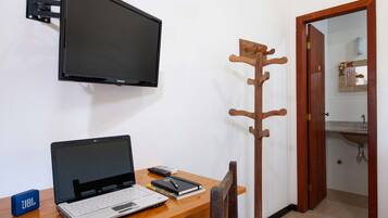 Una habitación con escritorio, laptop, televisor montado en la pared y perchero de madera.