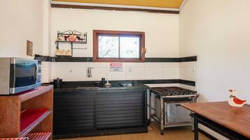 A compact kitchen with a microwave, stove, and sink. There's a window above the sink and a sign on the wall.