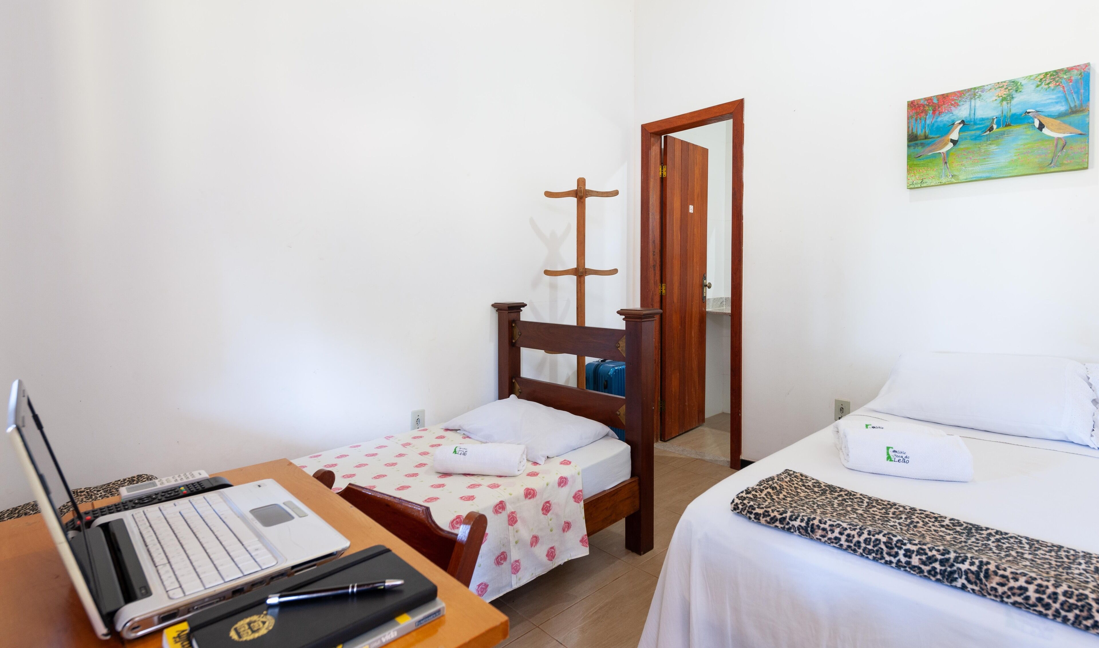 Un dormitorio con una cama de madera, un escritorio con una computadora portátil y un cuadro en la pared.