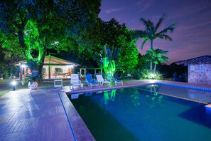 A swimming pool with lounge chairs, a covered seating area, and lush greenery. - SITIO TOCA DO LEAO (Guarapari)
