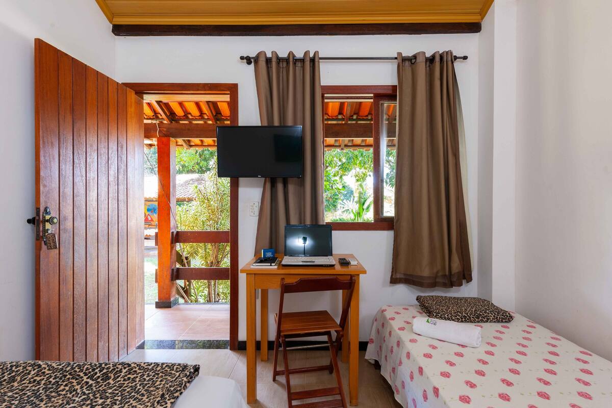 A room with a wooden desk, a laptop, a TV, and two beds with patterned bedsheets.