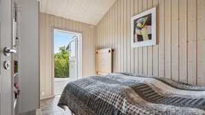 A bedroom with a bed, a door, a window, and a framed picture on the wall.