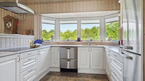 A modern kitchen with white cabinetry, stainless steel appliances, and large windows offering a view of greenery.